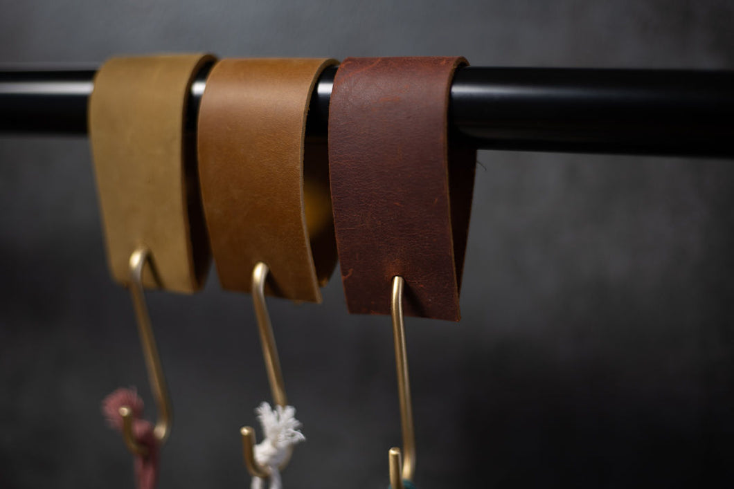 three leather straps with brass hooks used to hang plant hangers over a curtain rod