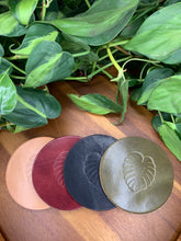 Load image into Gallery viewer, circular leather coaster burgundy black tan olive with a monstera  leaf stamped in the middle
