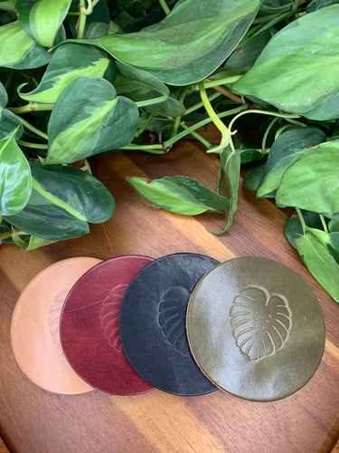 circular leather coaster burgundy black tan olive with a monstera  leaf stamped in the middle